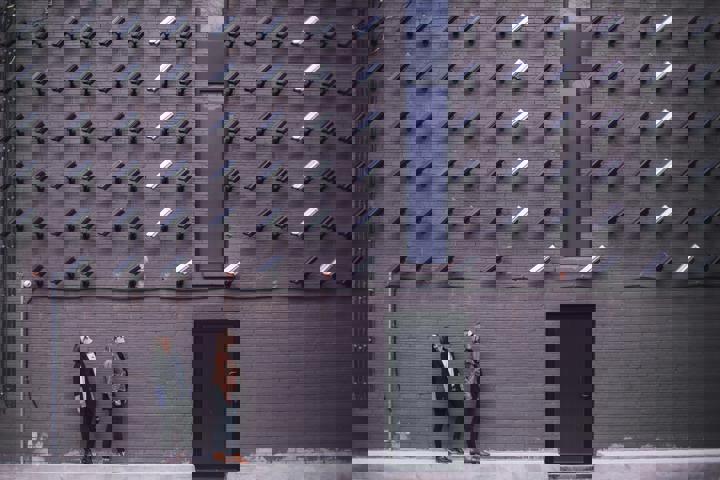Outside wall with many security cameras pointing down at 2 people at a door